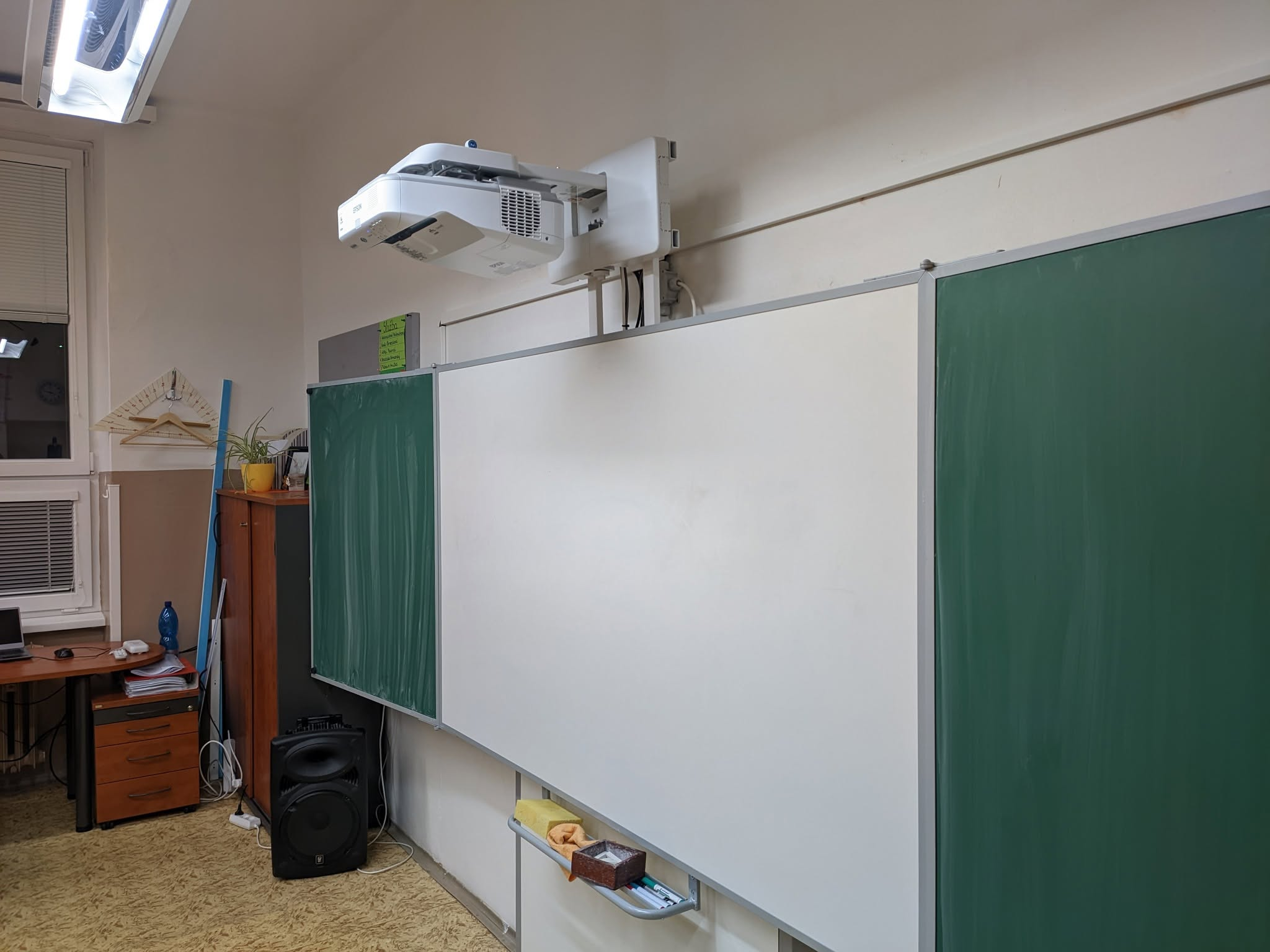 Projektor upevněný nad školní tabulí v učebně